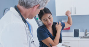 woman explaining shoulder pain to doctor in exam room